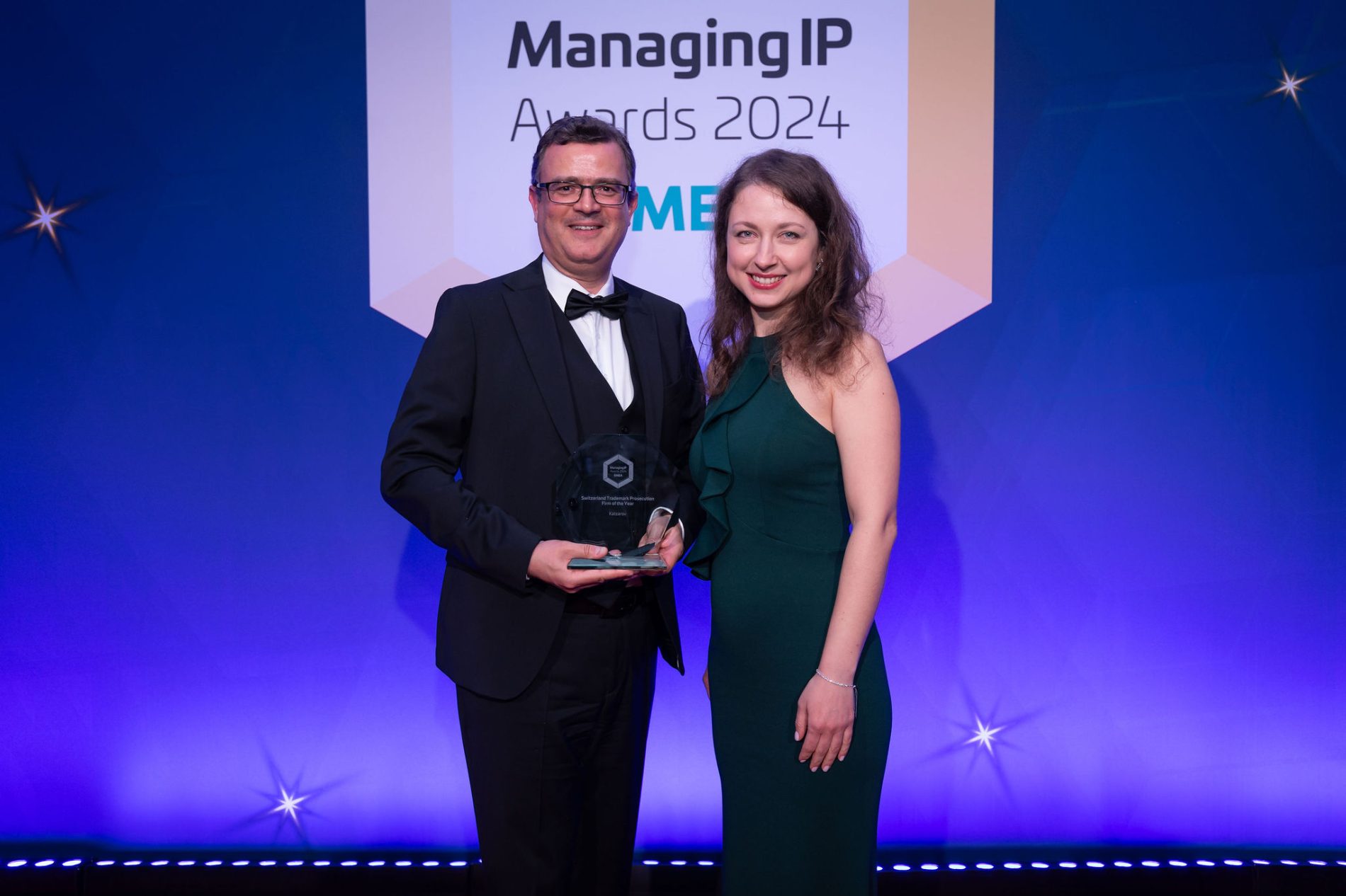 Two individuals in formal attire posing with an award at the Managing IP Awards 2024, with a backdrop highlighting the event.